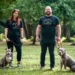 a man and a woman holding two XL bully dogs